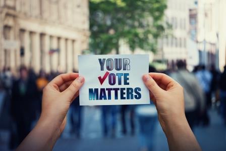 An image of a person holding a sticker that says "Your Vote Matters"