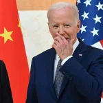 President Joe Biden standing in front of United States and China flags