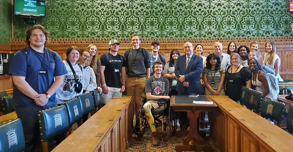 Students pose for a photo in the committee room of the Houses of Parliament with MP Hywel Williams.