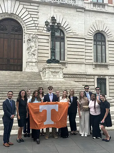 UT students posing for a photo in front of steps while holding a UT flag