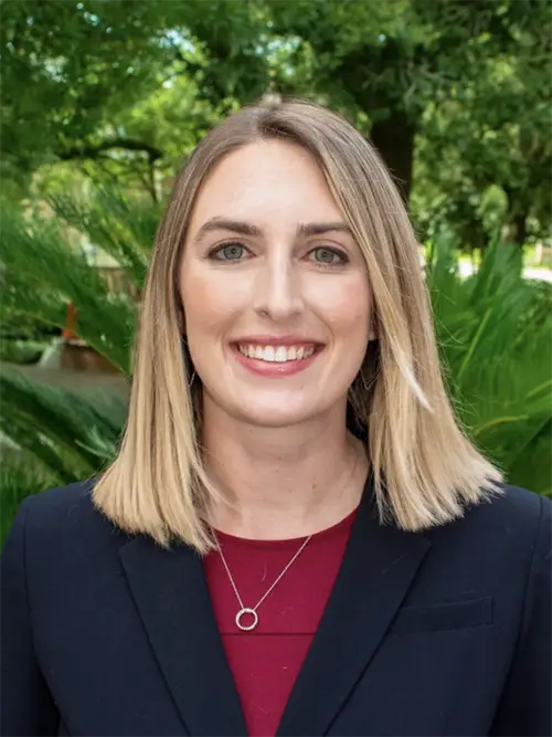 Headshot phot of a woman in professional dress with outdoor greenery behind her