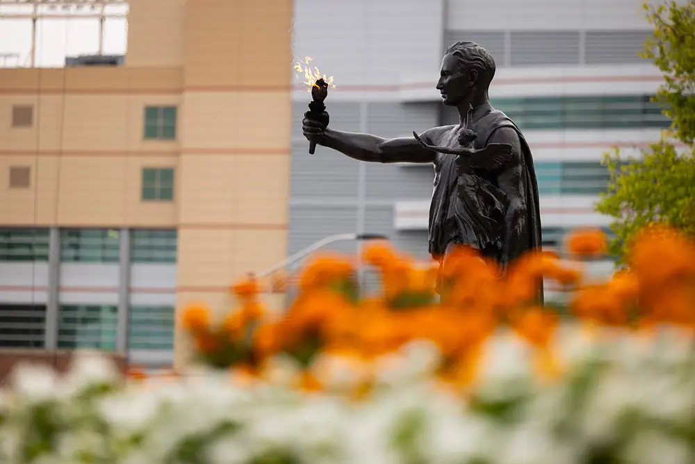 UT's Torchbearer holds an open flame in front of orange flowers.